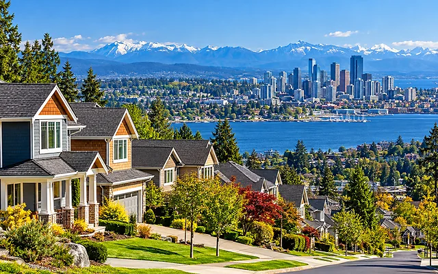 Best places to live in the U.S. featuring a sunny residential neighborhood overlooking a waterfront city skyline and distant snow-capped mountains.